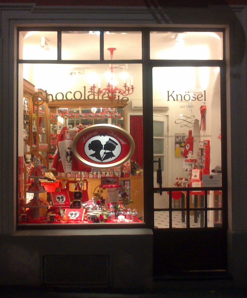 Beleuchtetes Schaufenster des Café Knösel in Heidelberg, dekoriert mit Heidelberger Studentenküssen