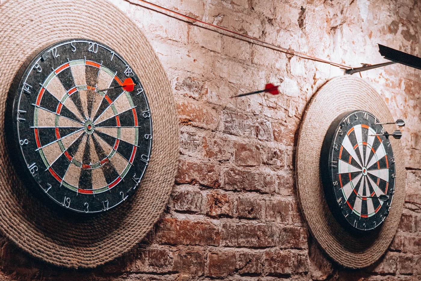 Zwei Dartscheiben mit Pfeilen an einer Backsteinwand